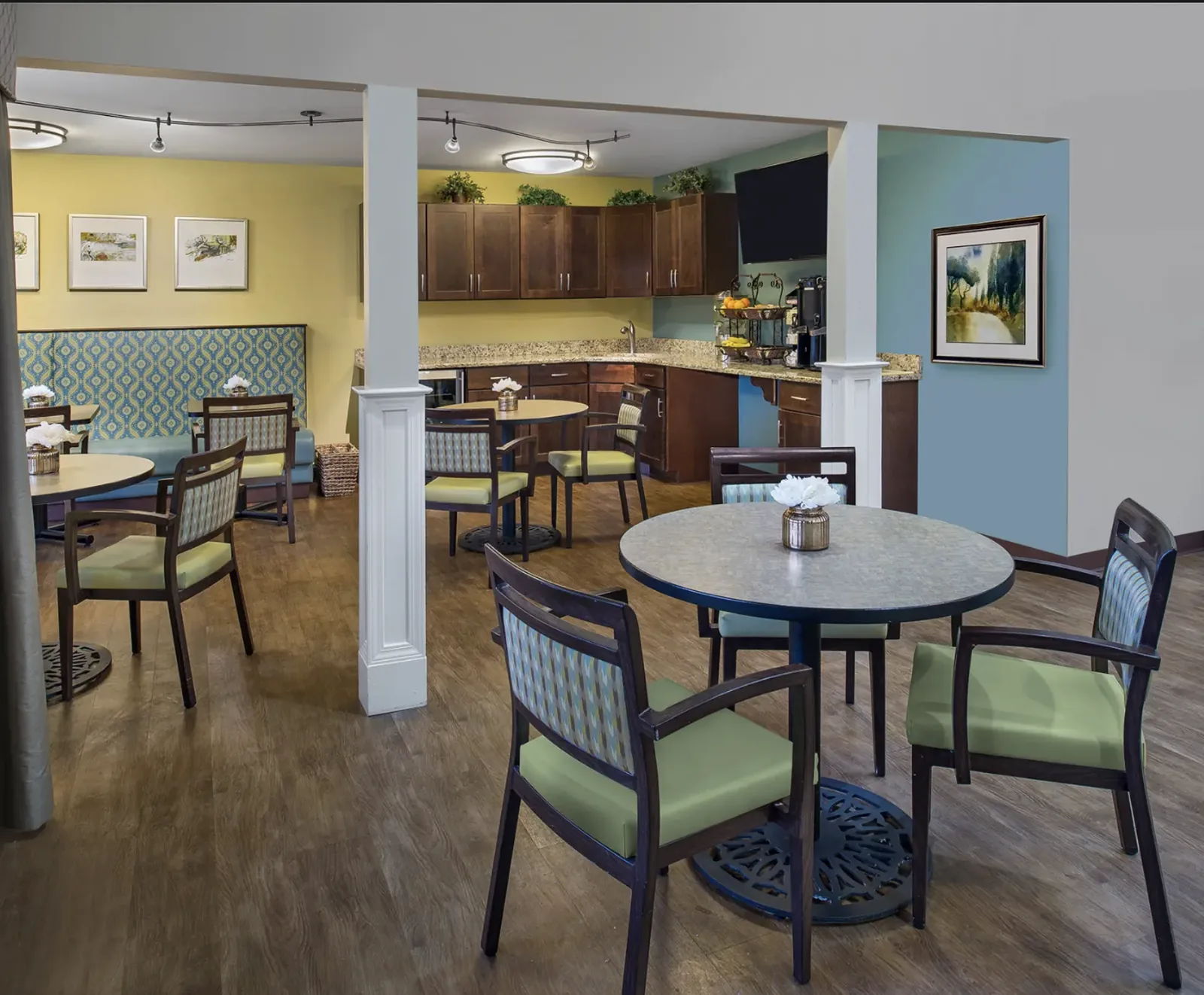 The bistro: café tables and green upholstered chairs beside the coffee counter at Comfort Cove Senior Living in West Bloomfield, MI