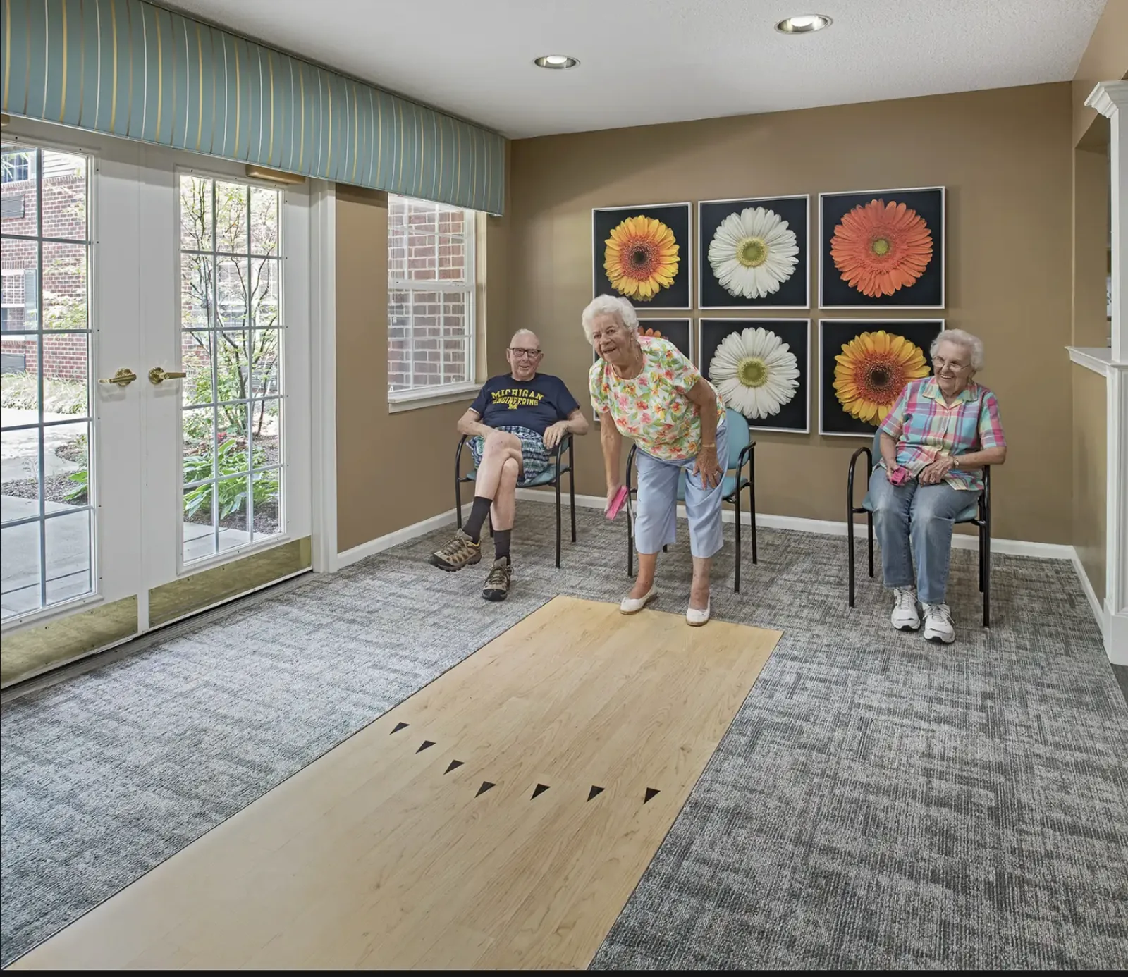 A resident bowling on the indoor lane while friends watch at Comfort Cove Senior Living in West Bloomfield, MI