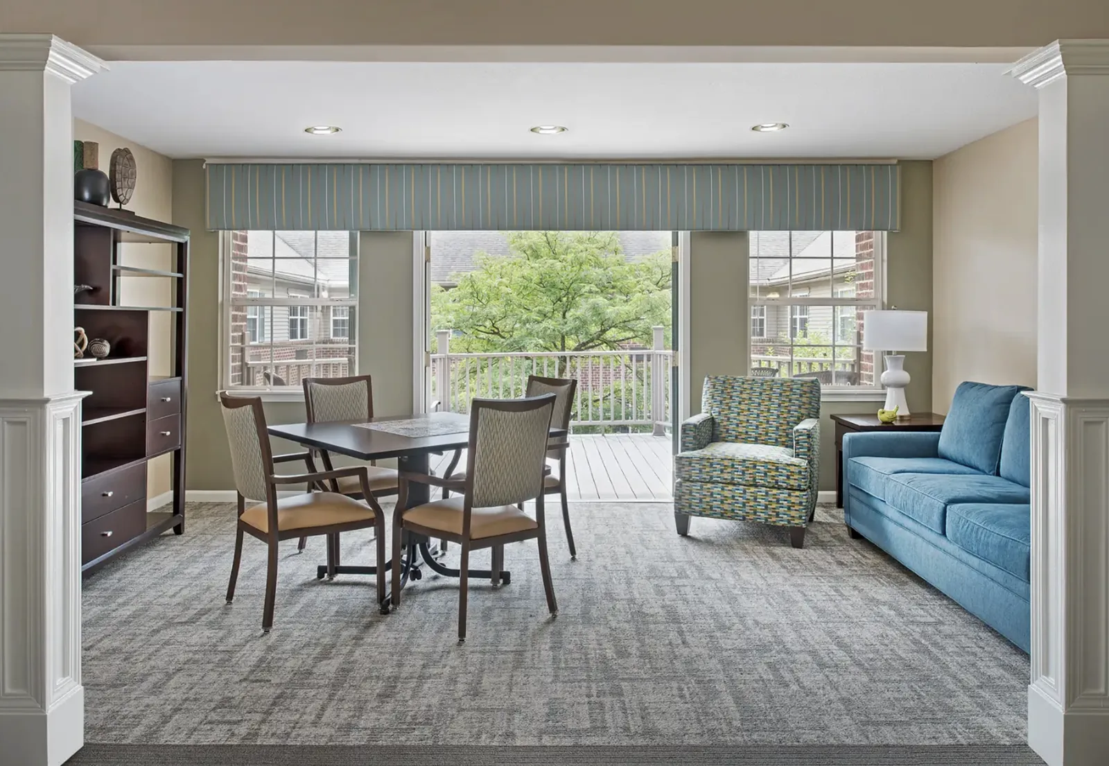 A common room: games table by the doors to the deck, a patterned armchair and a blue sofa at Comfort Cove Senior Living in West Bloomfield, MI