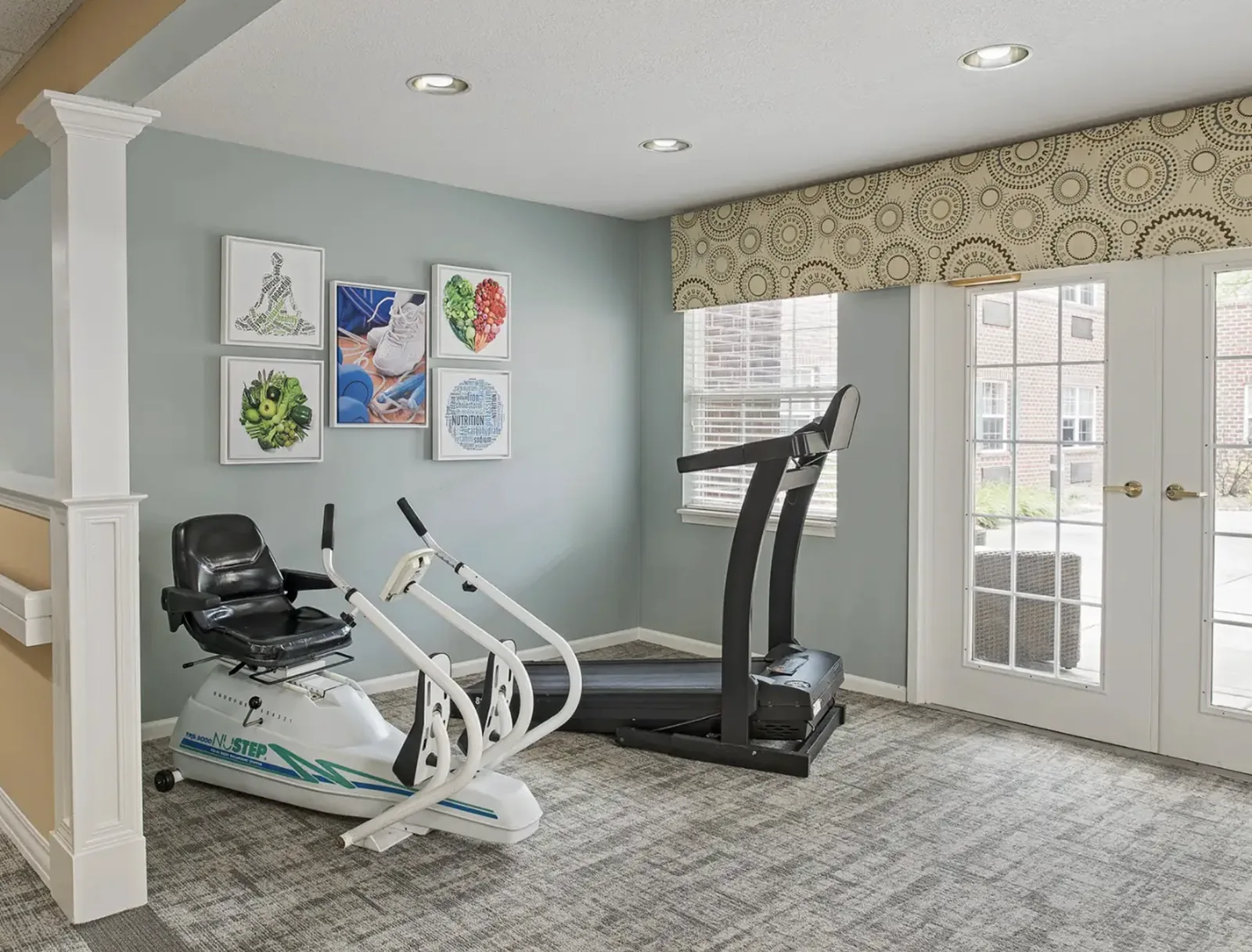 The fitness room, with a NuStep recumbent trainer and treadmill by the patio doors at Comfort Cove Senior Living in West Bloomfield, MI