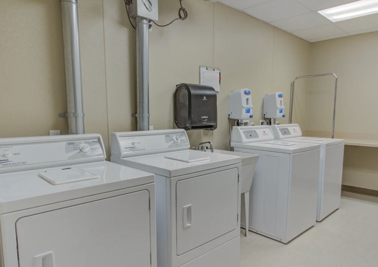 The laundry room: two washers and two dryers with a folding counter and hanging rail at Comfort Cove Senior Living in West Bloomfield, MI