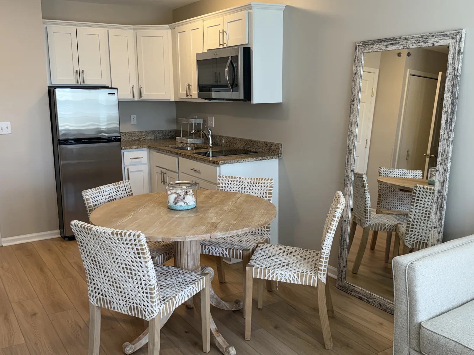 A furnished apartment: kitchenette and round dining table with woven chairs at Comfort Cove Senior Living in West Bloomfield, MI